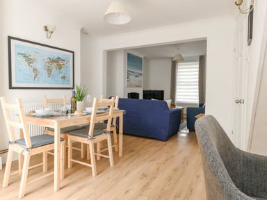 A dining area with a wooden table and chairs next to a living room with blue sofas and a television at Day Cottage in Weymouth
