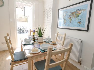 A dining area with a wooden table set with bowls plates wine bottle and an aloe plant with chairs and a world map on the wall at Day Cottage Weymouth