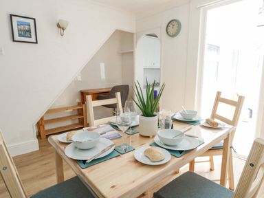 A dining table set with white plates bowls bread and glasses with a green plant in the center at Day Cottage in Weymouth