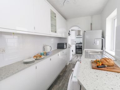 A kitchen with white cabinets a gray countertop a sink a loaf of bread on a cutting board and an archway leading to a cooking area at Day Cottage in Weymouth
