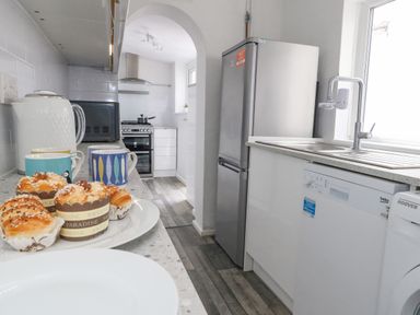 A kitchen with a countertop holding cupcakes mugs a kettle and a microwave a refrigerator a dishwasher a washing machine and a stove at Day Cottage in Weymouth