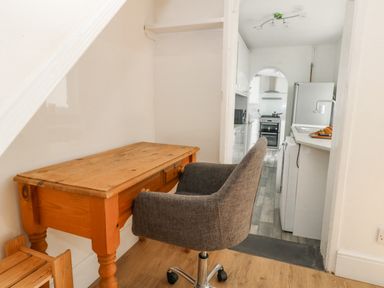 A wooden desk with a gray office chair next to a kitchen with white appliances at Day Cottage in Weymouth