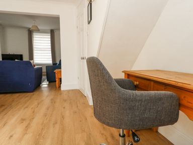 A wooden desk with a grey chair in a room with wooden flooring and blue sofas in an adjacent living area at Day Cottage in Weymouth