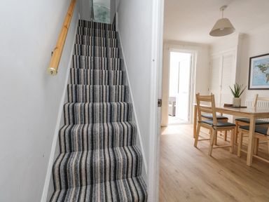 Staircase with striped carpet next to a dining area with wooden table and chairs at Day Cottage Weymouth