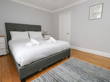 A bedroom with a grey upholstered bed and white bedding at Day Cottage in Weymouth