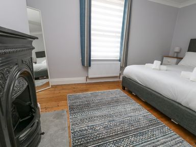 A bedroom with a bed side table and a mirror near a window with curtains at Day Cottage in Weymouth