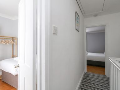 A hallway with striped carpet leading to two bedrooms with beds and wooden floors at Day Cottage in Weymouth