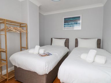 A bedroom with two single beds with white bedding a wooden clothes rack and a framed picture on the wall at Day Cottage in Weymouth