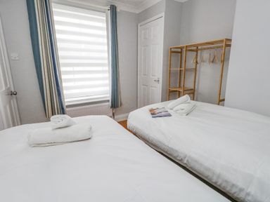 A bedroom with two beds white towels on beds wooden clothes rack by wall at Day Cottage Weymouth