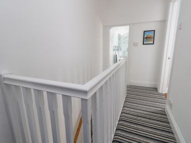 A hallway with white railing and striped carpet leading to a bathroom with marble walls at Day Cottage in Weymouth