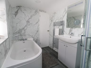 A bathroom with a bathtub sink mirror towel rack and shower at Day Cottage in Weymouth