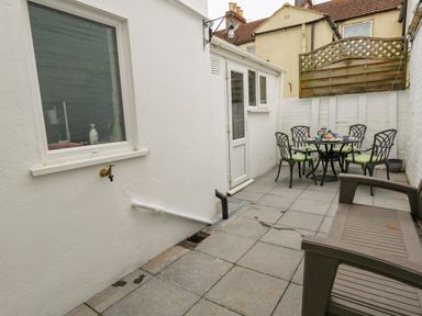 A paved outdoor patio area with a table set and chairs and a bench at Day Cottage in Weymouth