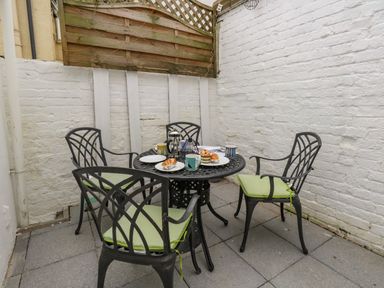 An outdoor patio area with a round metal table and four chairs with green cushions at Day Cottage in Weymouth