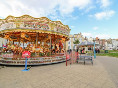 A carousel with painted horses in a paved outdoor area near buildings and a kiosk at Day Cottage in Weymouth