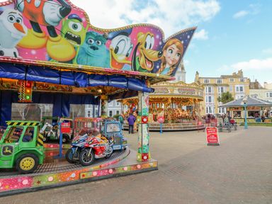 Children's rides with cartoon character decorations and a carousel in an outdoor area with buildings in the background at Day Cottage in Weymouth