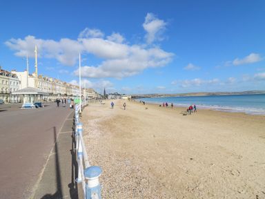 A sandy beach with people walking near the water and a row of buildings along a promenade at Day Cottage in Weymouth