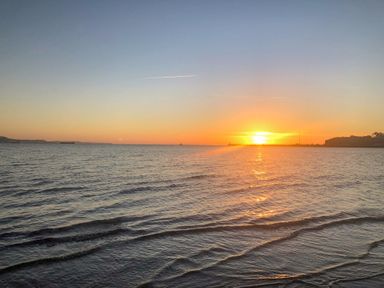A sunset over the sea with gentle waves and land on the horizon at Day Cottage in Weymouth