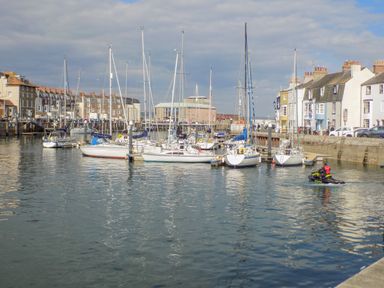 Sailboats docked in a harbor with buildings along the waterfront and a person on a jet ski in the water at Day Cottage in Weymouth