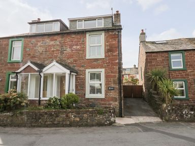 A stone house with green window frames and small garden in front at Wainwright Cottage in Gosforth