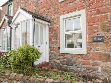 The exterior of a stone cottage with a white door porch and a window beside a small garden at Wainwright Cottage in Gosforth