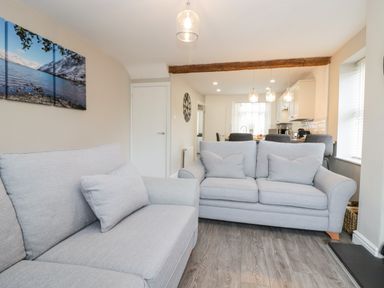A living room with two gray sofas and a wooden beam with a kitchen in the background at Wainwright Cottage in Gosforth