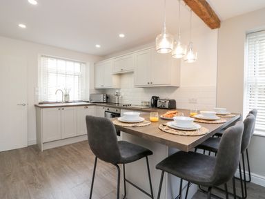 A kitchen with a dining counter set with plates and glasses and bar stools at Wainwright Cottage in Gosforth