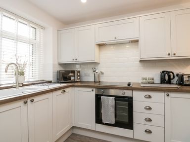 A kitchen with white cabinets wooden countertops a microwave oven and a kettle at Wainwright Cottage in Gosforth