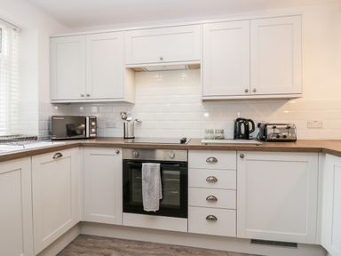 A kitchen with white cabinets a microwave oven kettle toaster and cooking utensils at Wainwright Cottage in Gosforth