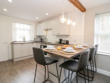 A kitchen with a wooden floor island and four chairs set with plates bowls glasses and orange juice at Wainwright Cottage in Gosforth