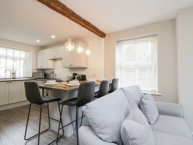 A kitchen area with a wooden countertop island and bar stools next to a sofa by a window at Wainwright Cottage in Gosforth