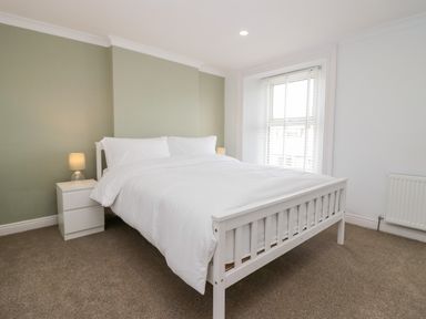 A bedroom with a white bed and nightstand with lamps by a window at Wainwright Cottage in Gosforth