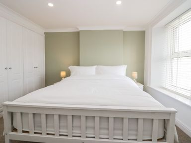 A bedroom with a white bed frame a white bed two bedside tables with lamps built in white wardrobes and a window with blinds at Wainwright Cottage in Gosforth