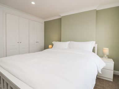 A bedroom with a bed with white bedding two bedside tables with lamps and white built in wardrobes at Wainwright Cottage in Gosforth