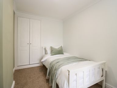 A small bedroom with a single bed white bedding a green pillow and blanket and a built in wardrobe at Wainwright Cottage in Gosforth