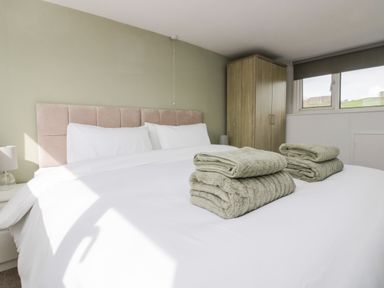 A bedroom with a bed with white linens and folded towels a wardrobe and a window at Wainwright Cottage in Gosforth