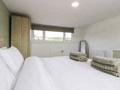 A bedroom with a white bed and folded green towels on it next to a wooden wardrobe and window with a gray blind at Wainwright Cottage in Gosforth