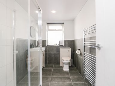 A bathroom with a shower enclosure sink toilet towel rack and window at Wainwright Cottage in Gosforth