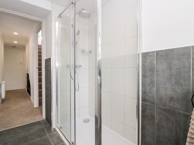 A bathroom with a glass shower enclosure and tiled walls next to a hallway and stairs at Wainwright Cottage in Gosforth