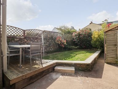 A garden with a wooden deck and table with chairs a stone wall with lattice fencing and a wooden shed at Wainwright Cottage in Gosforth