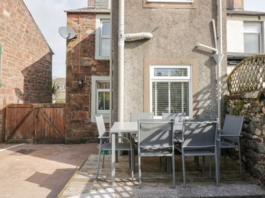 A patio area with a six-seat outdoor dining table and chairs outside a stone and stucco building at Wainwright Cottage in Gosforth