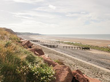 A beach with sand, rocks, and wooden groynes along the shore with grassy cliffs on the left