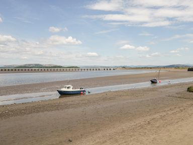 A river estuary with two boats on the sand and a long bridge in the background at Wainwright Cottage in Gosforth