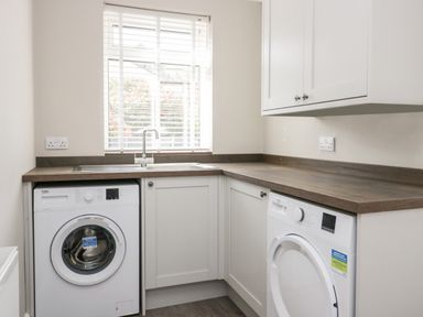 A laundry room with a washing machine and dryer under a wooden countertop and white cabinets at Wainwright Cottage in Gosforth