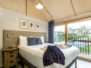 A bedroom with a double bed beside a wooden nightstand and large glass sliding doors overlooking a garden at Lodge 3 in Corfe Castle