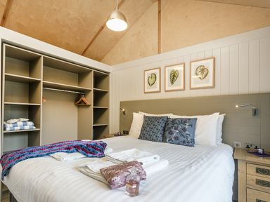 A bedroom with a bed pillows bedside tables open closet with hangers and blankets at Lodge 3 in Corfe Castle