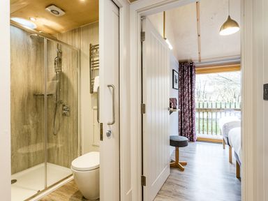 A bathroom with a shower and toilet next to a bedroom with two beds and a window with curtains at Lodge 3 in Corfe Castle