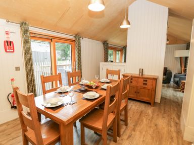 A dining area with a wooden table and six chairs set with plates and glasses in a room with wooden flooring and sliding glass doors at Lodge 6 in Corfe Castle