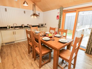 A kitchen and dining area with a wooden table and six chairs set with plates and glasses at Lodge 6 Corfe Castle