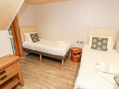 A bedroom with two single beds pillows and towels a wooden nightstand and a small wooden stump table at Lodge 6 in Corfe Castle