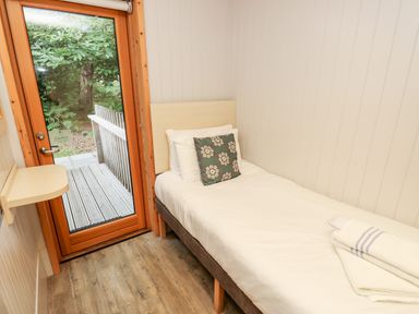 A small bedroom with a single bed next to a glass door showing a wooden deck outside at Lodge 6 in Corfe Castle